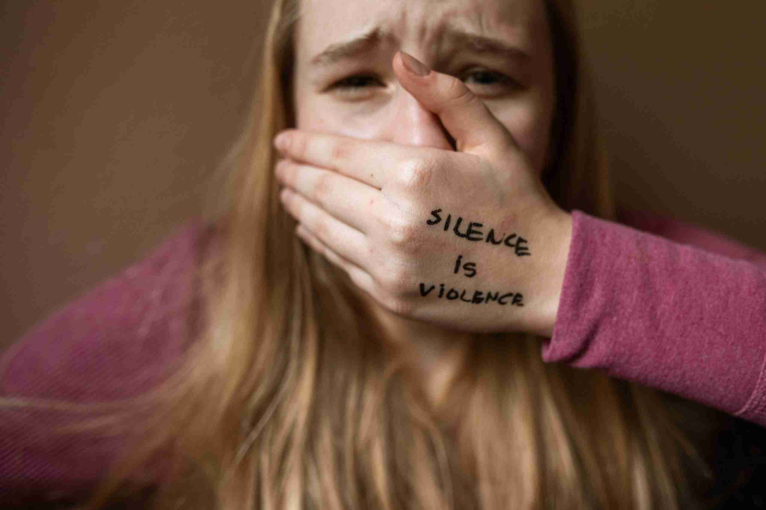 A woman holding her hand over her mouth with the words "Silence is violence" written on her hand