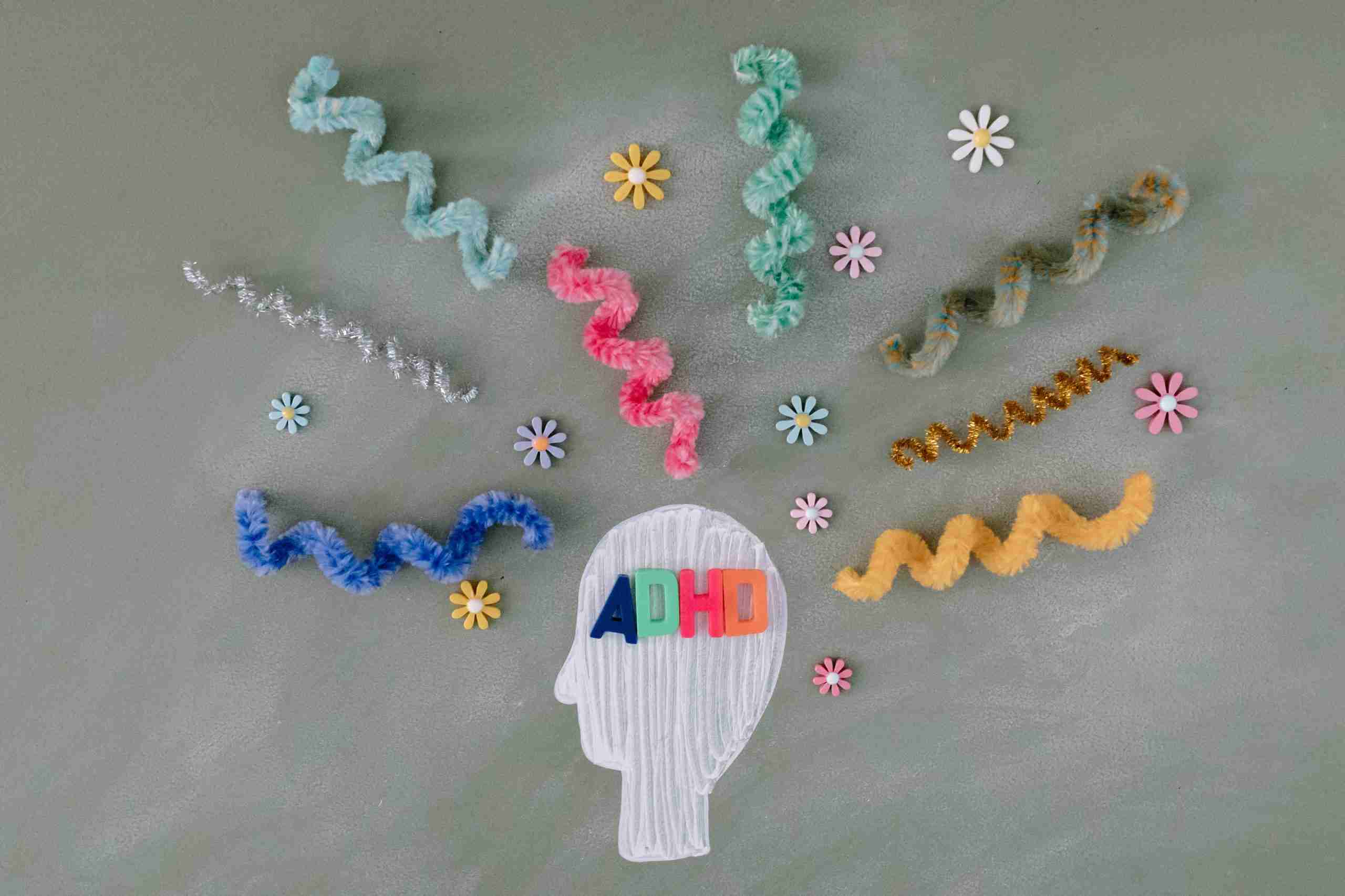 A painted head surrounded by squiggly pipe cleaners and flower stickers with the letters ADHD over the head in magnetic letters